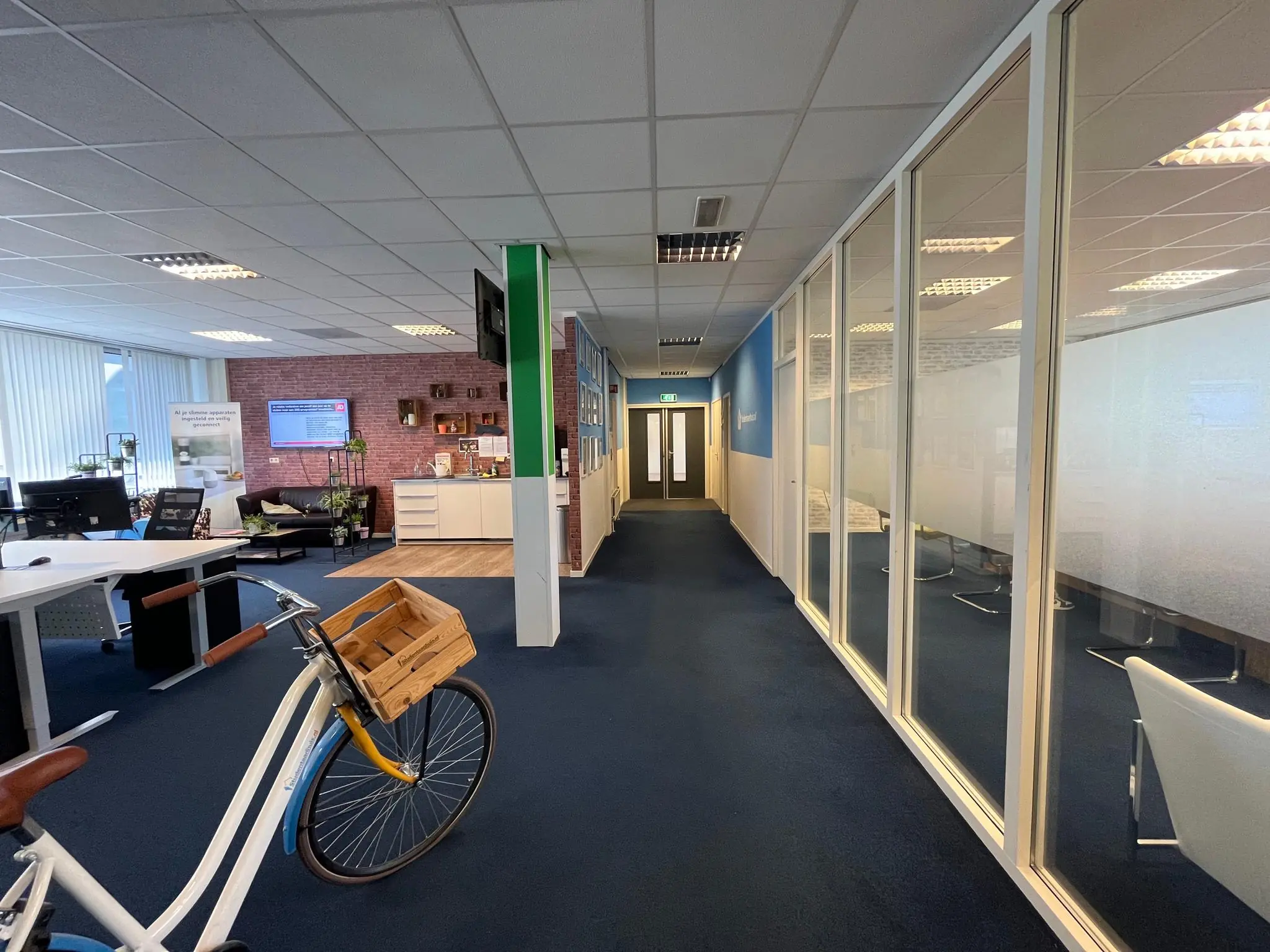 Kantoorruimte aan de Jan van Eycklaan met glazen vergaderruimtes, bureaus en een fiets met houten krat op de voorgrond.